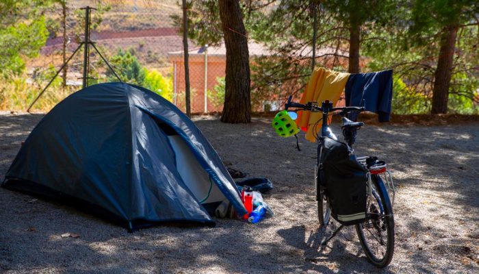 Tienda de campaña y bicicleta de cicloturismo en una parcela arbolada del Camping Albarracín